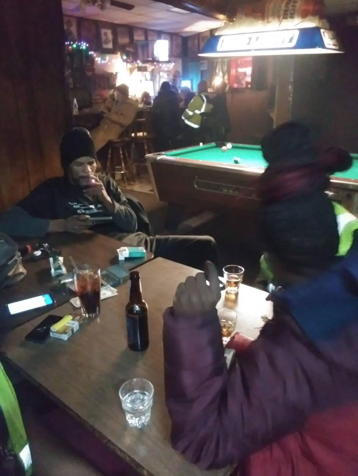 People drinking and smoking at a table inside The Ugly Broad.