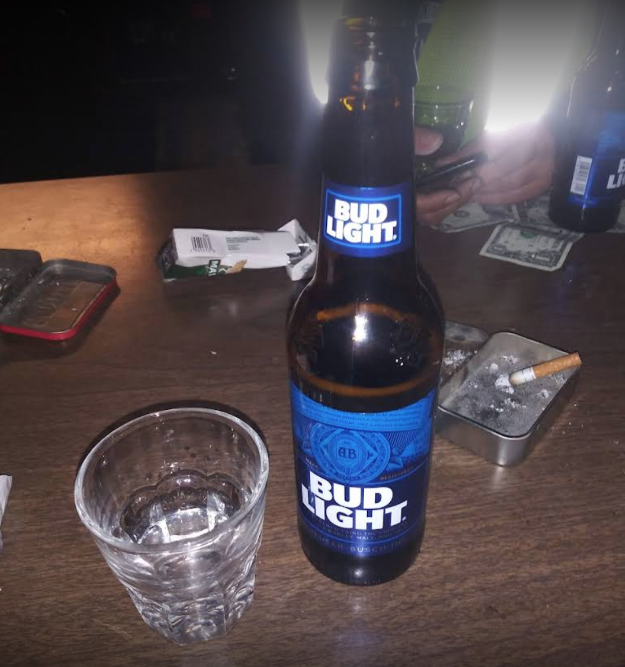 Close-up of a glass, a Bud Light bottle, and an ashtray on a table.
