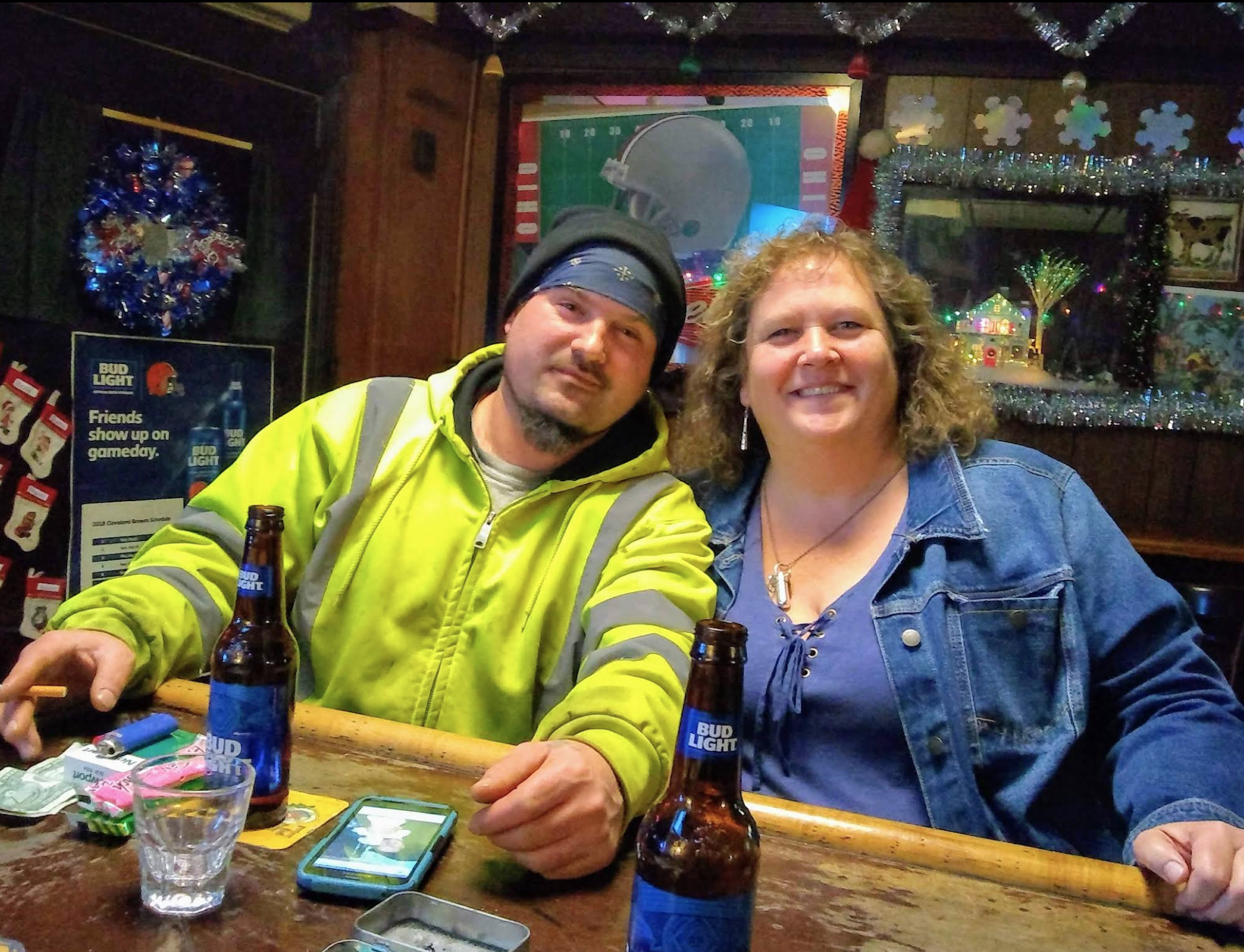Two people sitting at the bar with bottles of Bud Light in front of them.