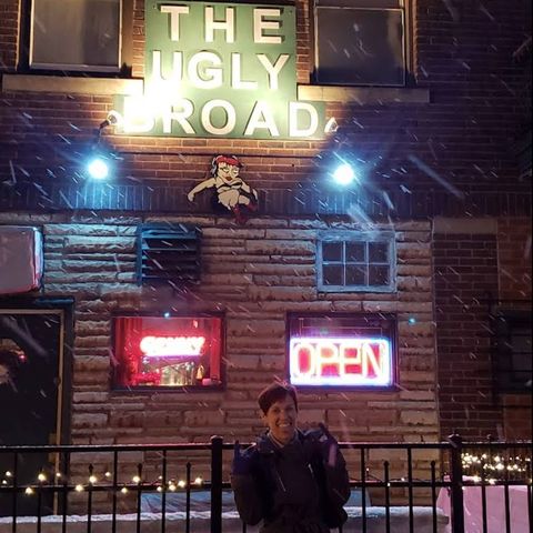 Exterior photo of a woman in front of The Ugly Broad sign while it snows.