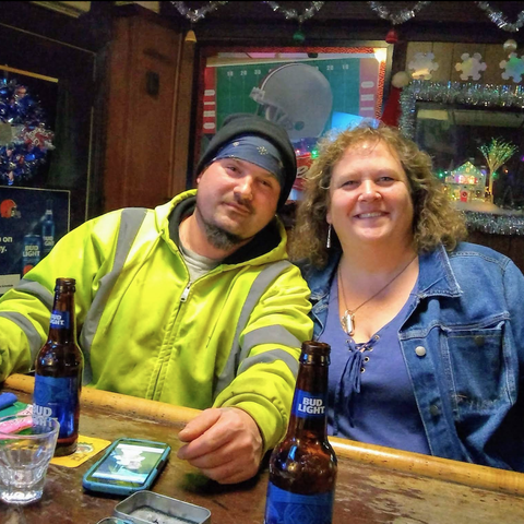 Two people sitting at the bar with bottles of Bud Light in front of them.