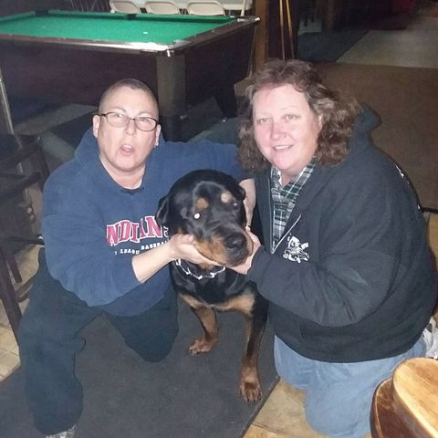 Two people with their arms around a dog.