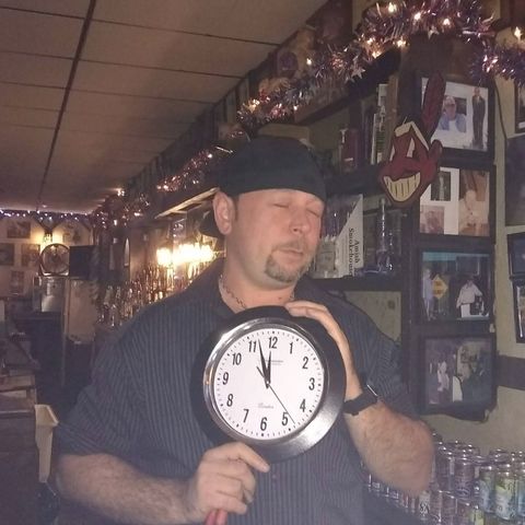 Man behind bar holding a clock.