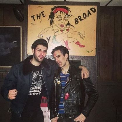 Two men standing in front of The Ugly Broad sign inside the bar.